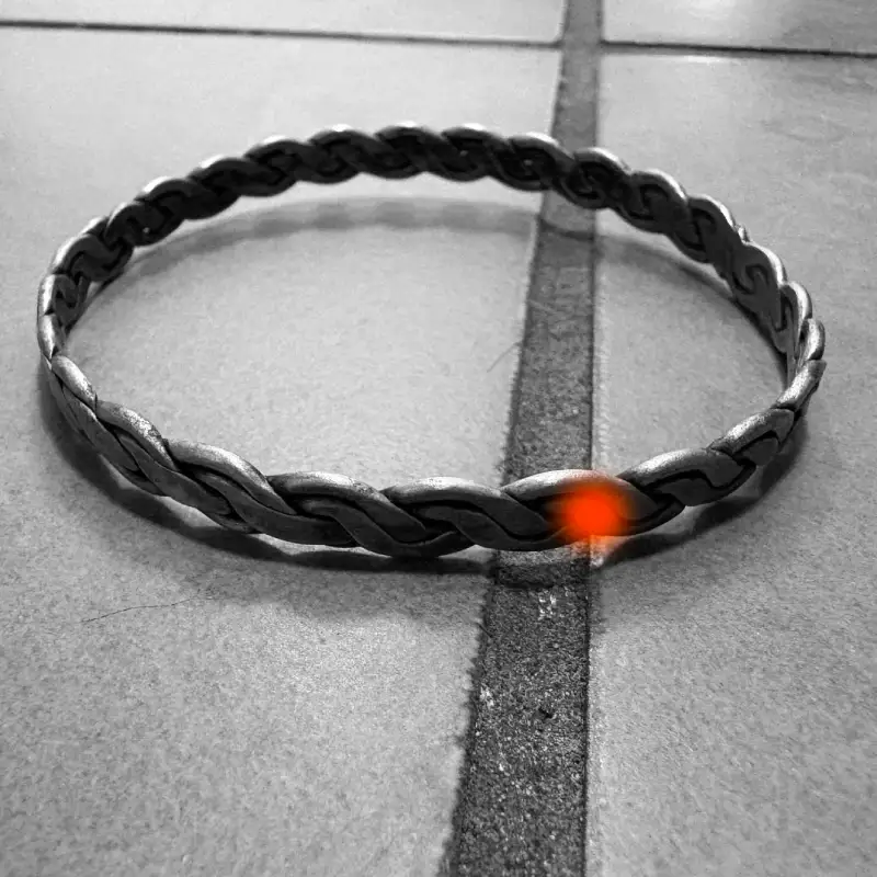 Silver braided bracelet on floor tiles with a small orange light embedded in the bracelet.