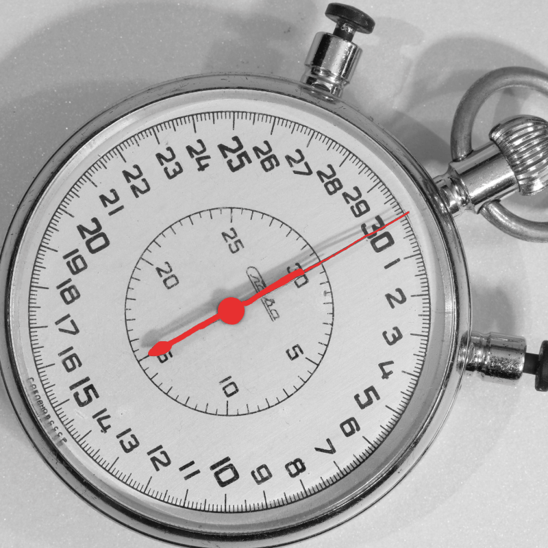Image is a black and white stopwatch with a red second hand pointing at thirty